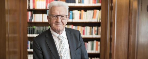 Ein Porträt von Winfried Kretschmann vor einer Bücherwand 