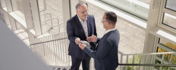 Netze BW-Kommunalberater Andreas Stampfer (r.) zeigt Bürgermeister Stefan Martus die Vorteile digitaler Wasserzähler. auf einer Treppe im Rathaus. 